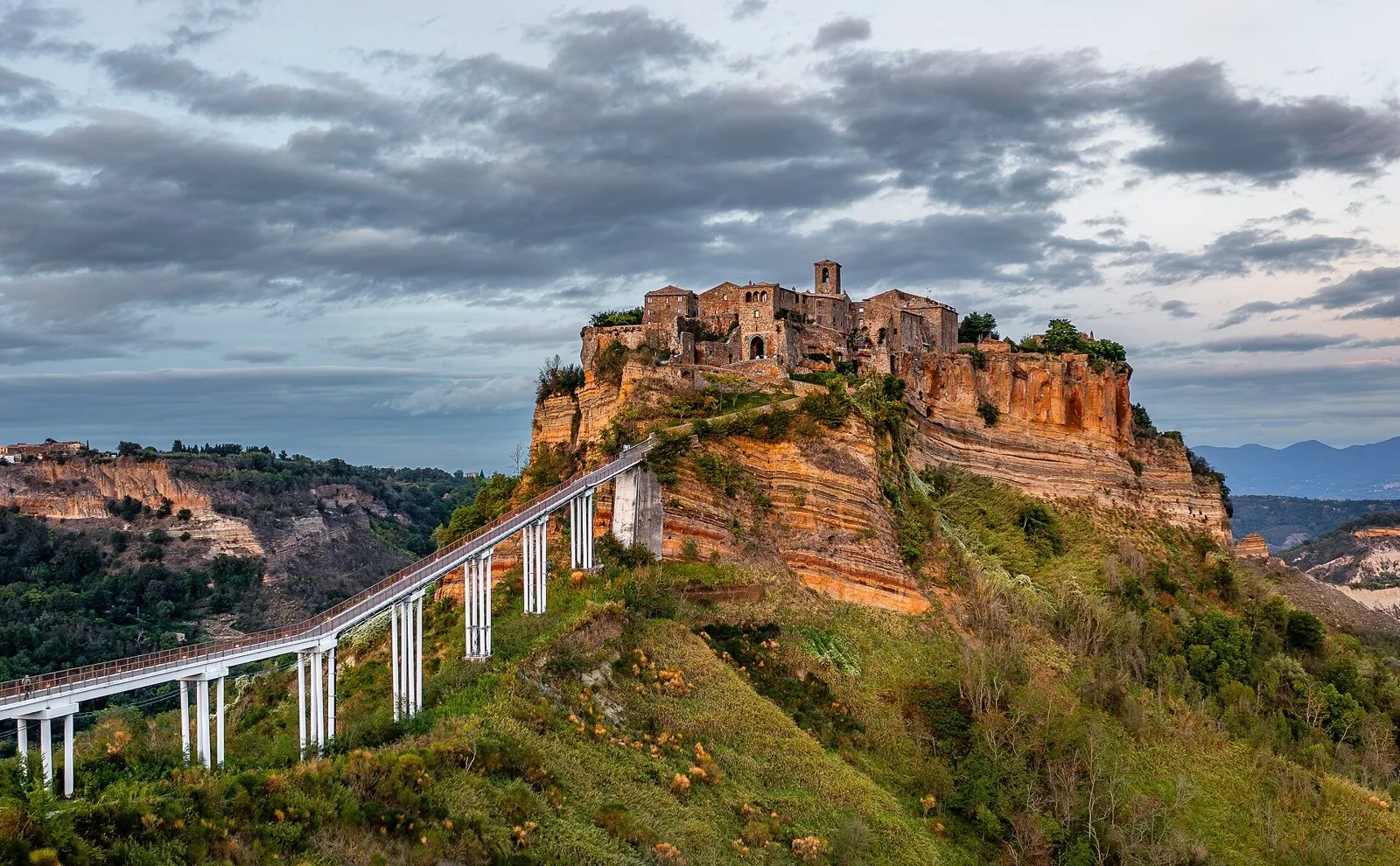 Civita di Bagnoregio sullo sperone di tufo con il ponte pedonale, sotto un cielo nuvoloso al tramonto