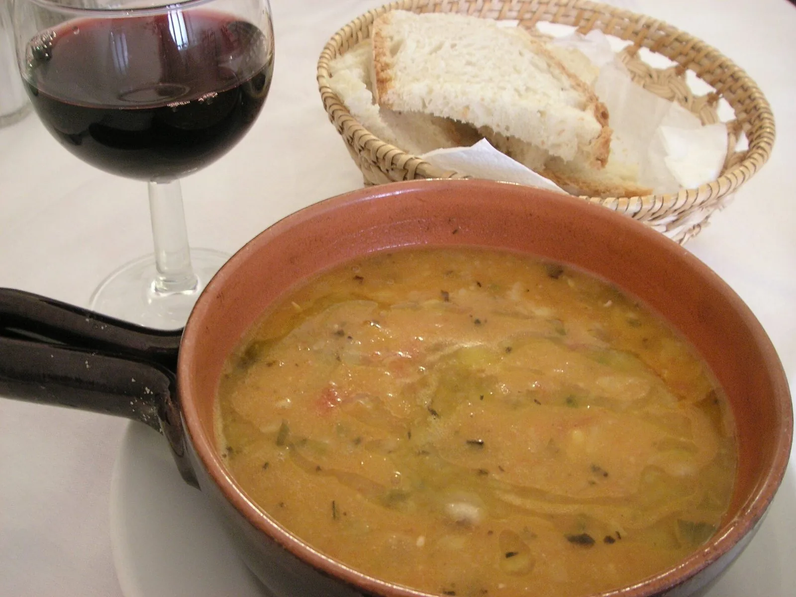 Zuppa di legumi e verdure in un tegame di coccio, con pane casereccio e un bicchiere di vino rosso
